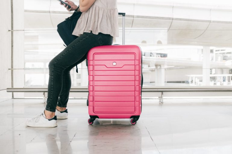 lady sitting on a pink checked-in suitcase